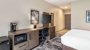 A hotel room with a bed, a desk with a microwave, a chair, a TV, and a coffee maker.