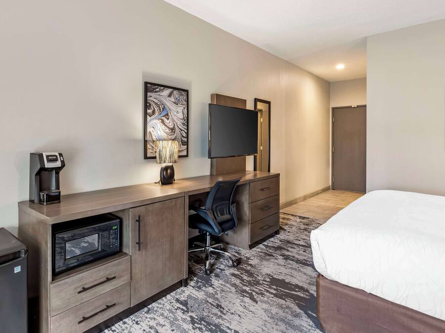 Une chambre d’hôtel équipée d’un lit, d’un bureau avec un micro-ondes, d’une chaise, d’une télévision et d’une machine à café.