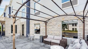 An outdoor patio with stone walls, a covered seating area, and a view of a modern building. - Best Western Plus Bourbonnais Hotel & Suites (Bourbonnais)