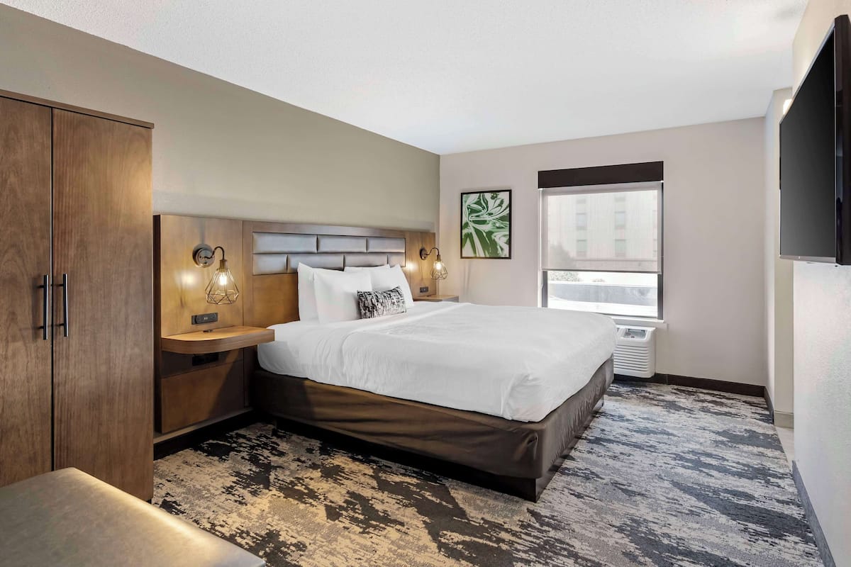 Une chambre d’hôtel avec un grand lit, une armoire en bois, des lampes de chevet, une fenêtre avec vue et un téléviseur à écran plat.