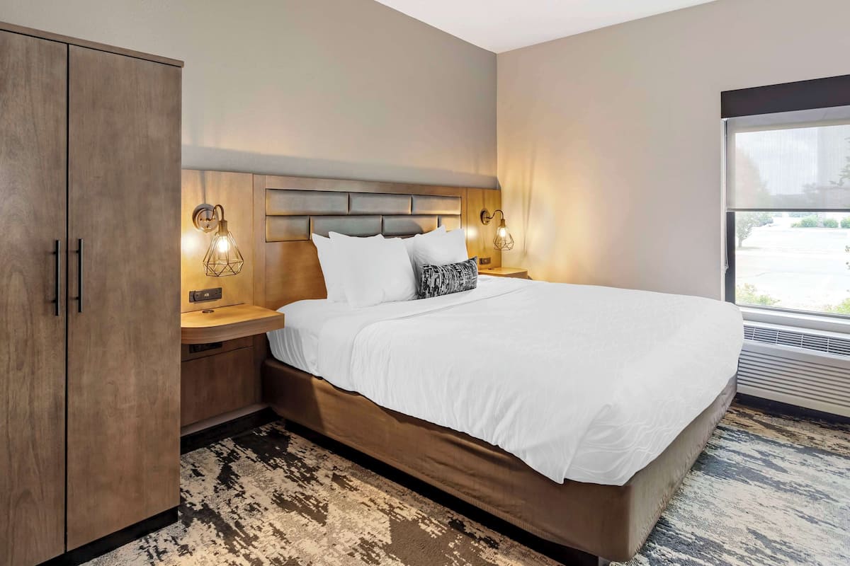 Une chambre d’hôtel avec un grand lit, une armoire en bois, des lampes de chevet et une vue par la fenêtre.