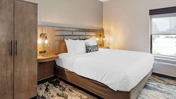 A hotel room with a large bed, wooden wardrobe, bedside lamps, and a view through a window.