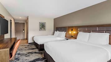 Quarto de hotel com duas camas, uma escrivaninha, uma cadeira, uma TV e um quadro na parede.
