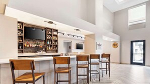 A modern bar area with wooden chairs, a counter with shelves of bottles, and a large flat-screen TV. - Best Western Plus Bourbonnais Hotel & Suites (Bourbonnais)