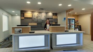 A reception desk with a digital display, a Holiday Inn Express sign, and a 7-Eleven convenience store in the background.