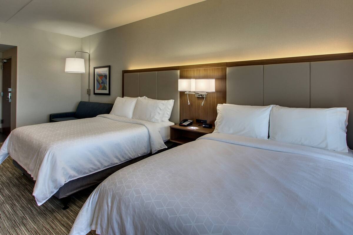 A hotel room with two beds, a bedside table with a lamp, a phone, and a painting on the wall.