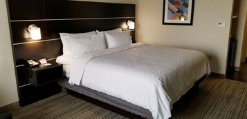 A hotel room with a large bed, a nightstand with a phone, and two wall-mounted lamps.
