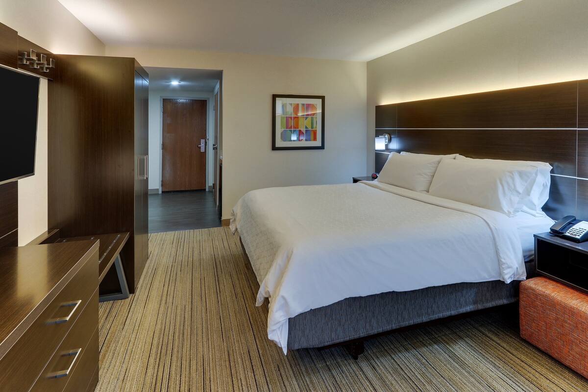 A hotel room with a large bed, a flat-screen TV, a desk, and a modern headboard.