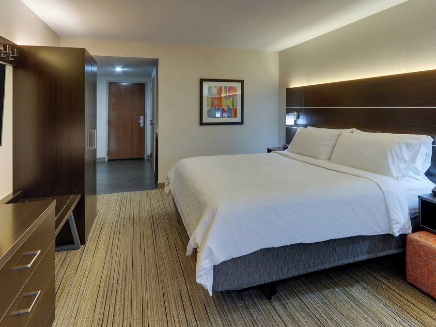 Une chambre d’hôtel avec un grand lit, un bureau, une télévision et une porte donnant sur un couloir.