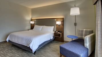 Ein Hotelzimmer mit einem großen Bett, einem Nachttisch mit Lampe, einem kleinen runden Tisch und einem Sessel.