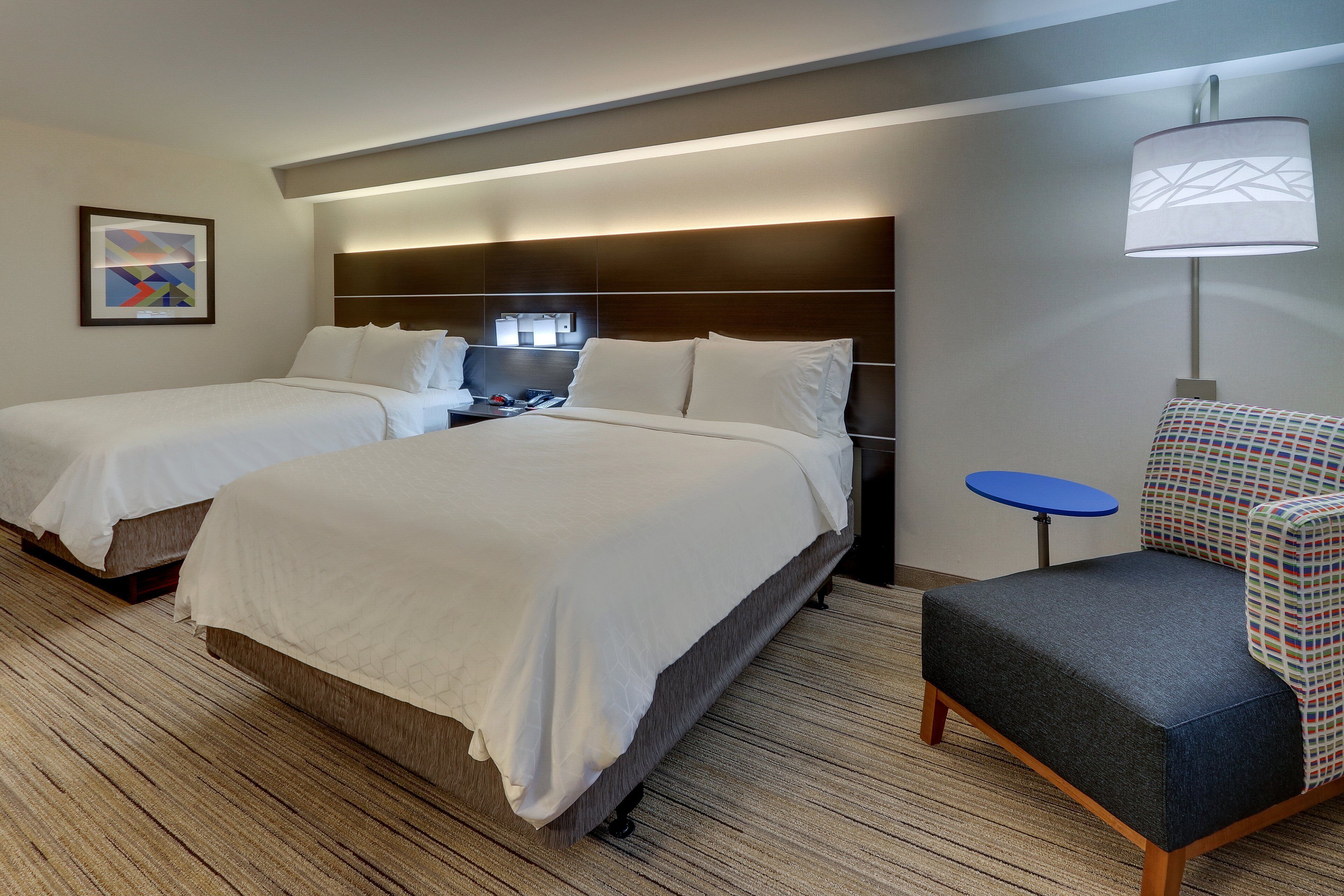 A hotel room with two beds, a desk, a chair, and a lamp.