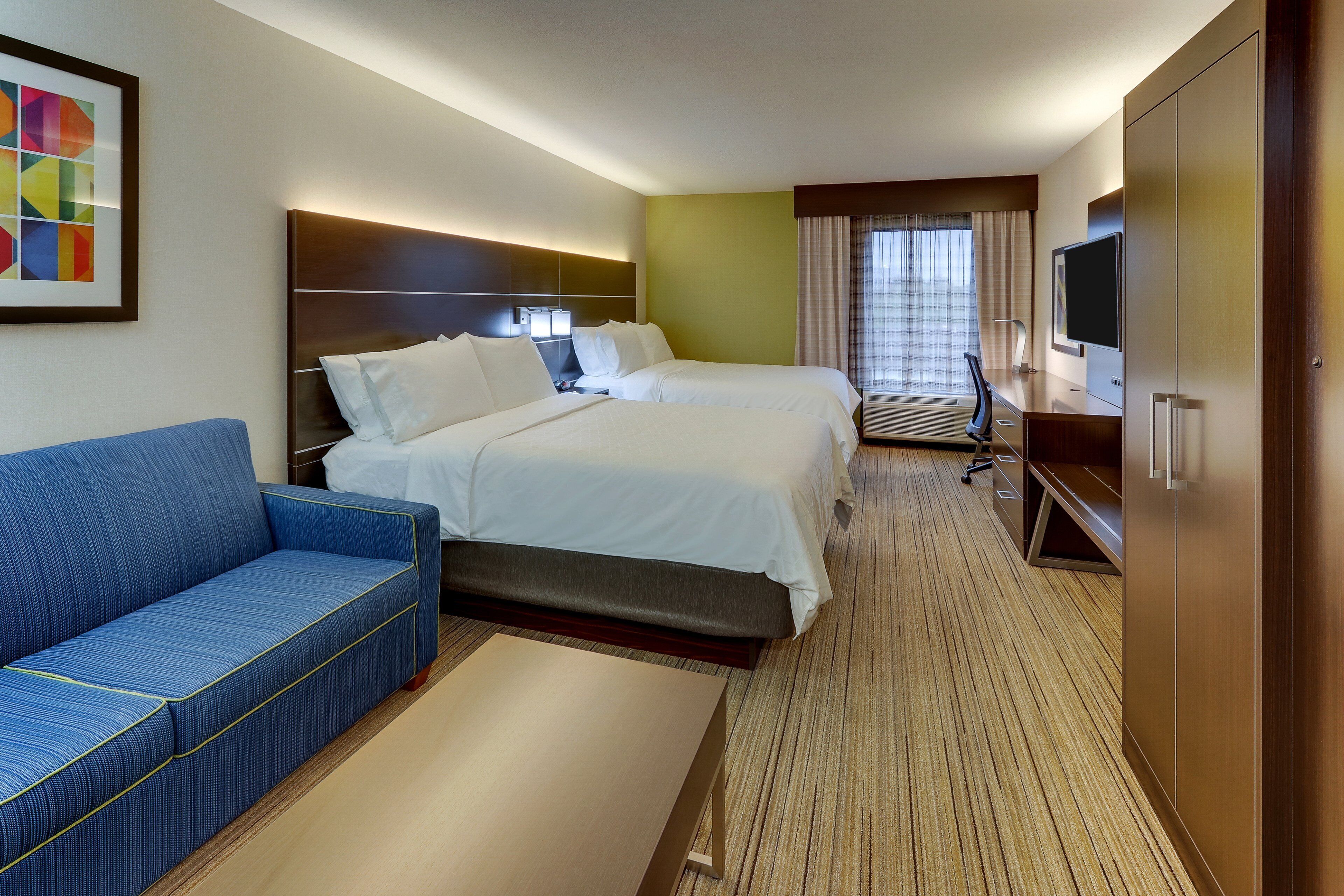 A hotel room with two beds, a sofa, a TV, and a desk.