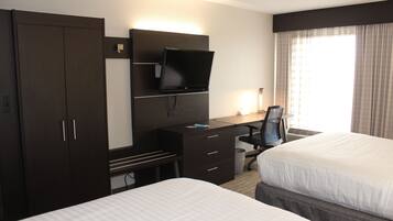 A hotel room with two beds, a desk with a computer, a television, and a wardrobe.