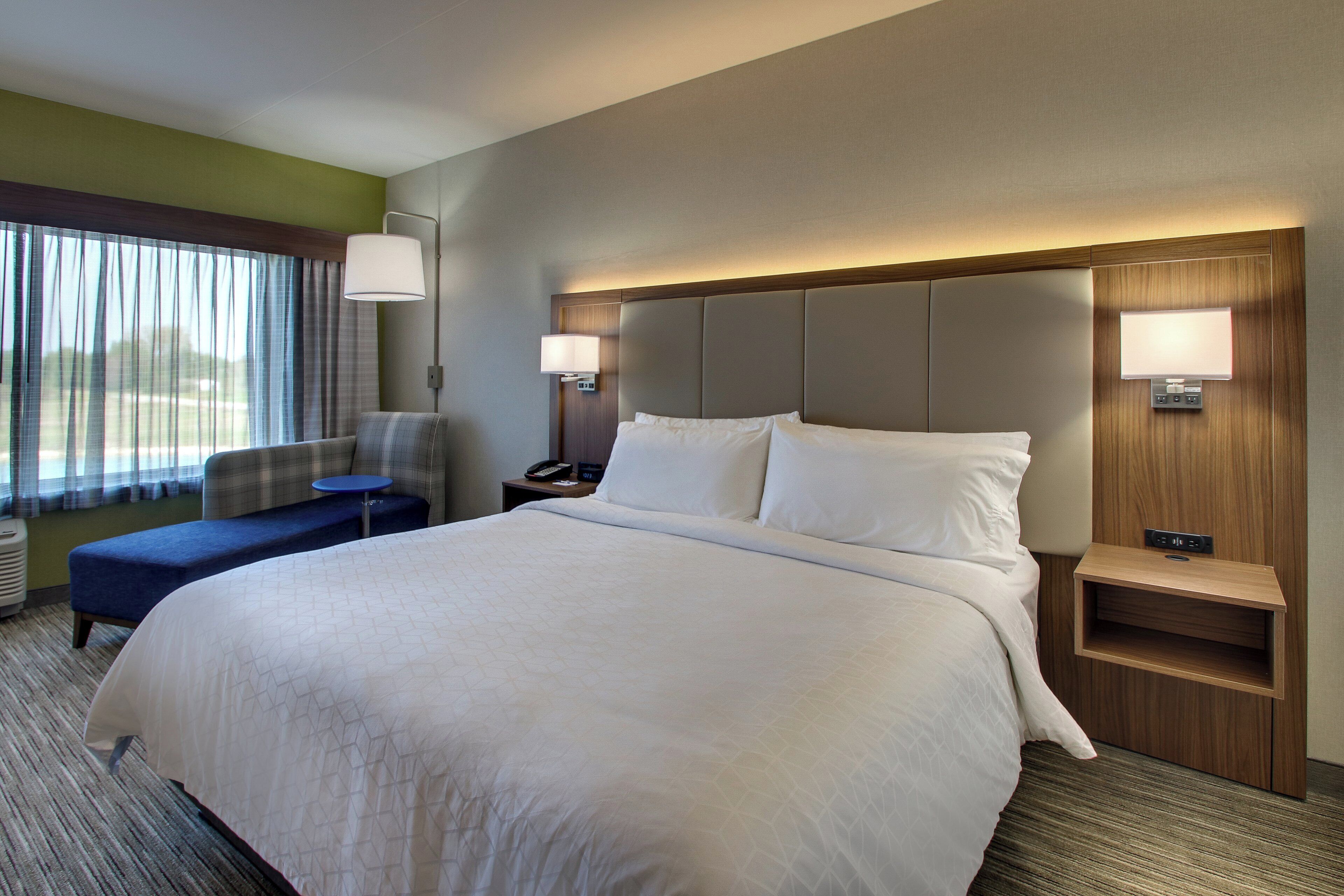 Une chambre d’hôtel avec un grand lit, un bureau, une chaise, une table de chevet et une fenêtre avec des rideaux.