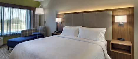 A hotel room with a large bed, a desk, a chair, a nightstand, and a window with curtains.