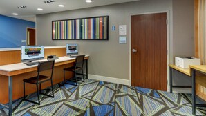 Un espace d’accueil d’hôtel comprenant deux postes de travail informatiques, une grande œuvre d’art rayée au mur et un panneau indiquant l’endroit où entreposer les bagages.
