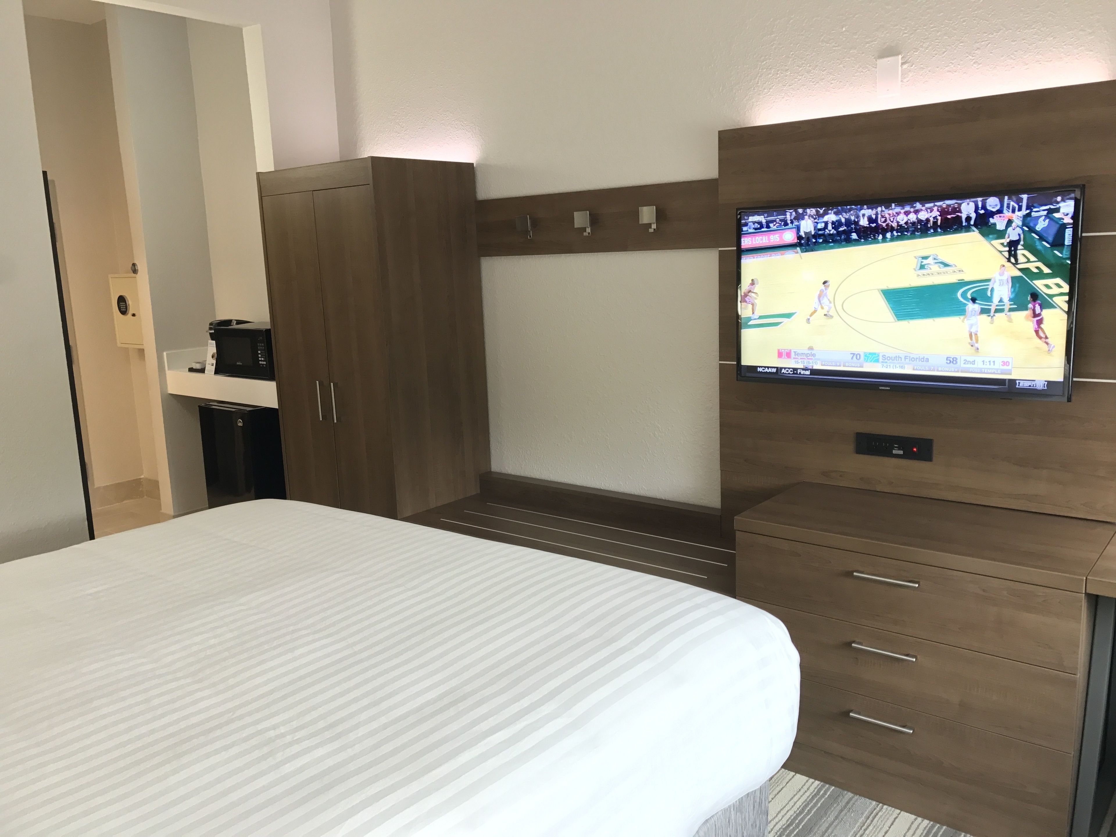 Camera d'albergo con un letto, una TV a muro, un armadio e una piccola scrivania con macchina per il caffè.