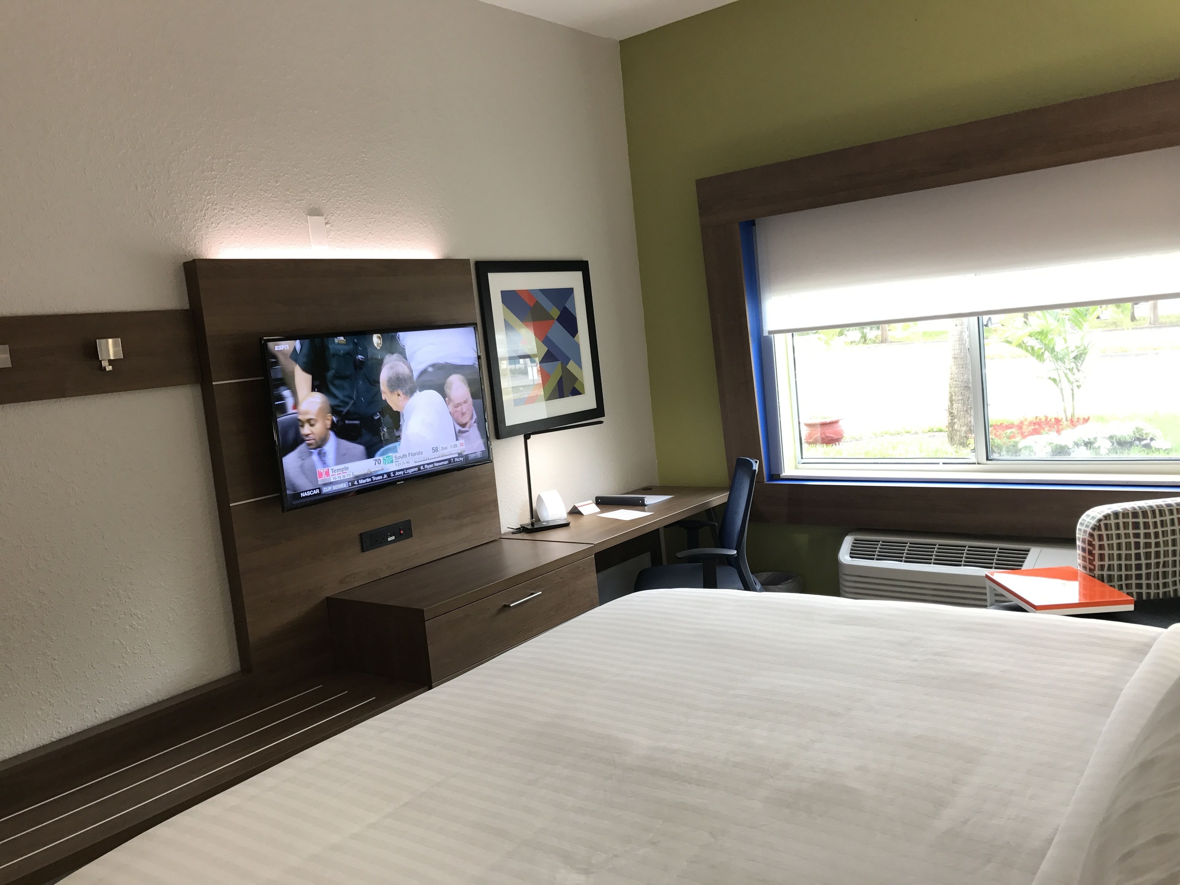 A hotel room with a bed, a desk with a computer, a television, and a window with a view of the outdoors.
