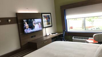 A hotel room with a bed, a desk with a computer, a television, and a window with a view of the outdoors.
