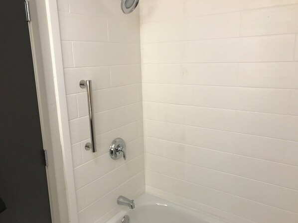 A bathroom with white tiled walls, a bathtub, and a shower area with a grab bar.