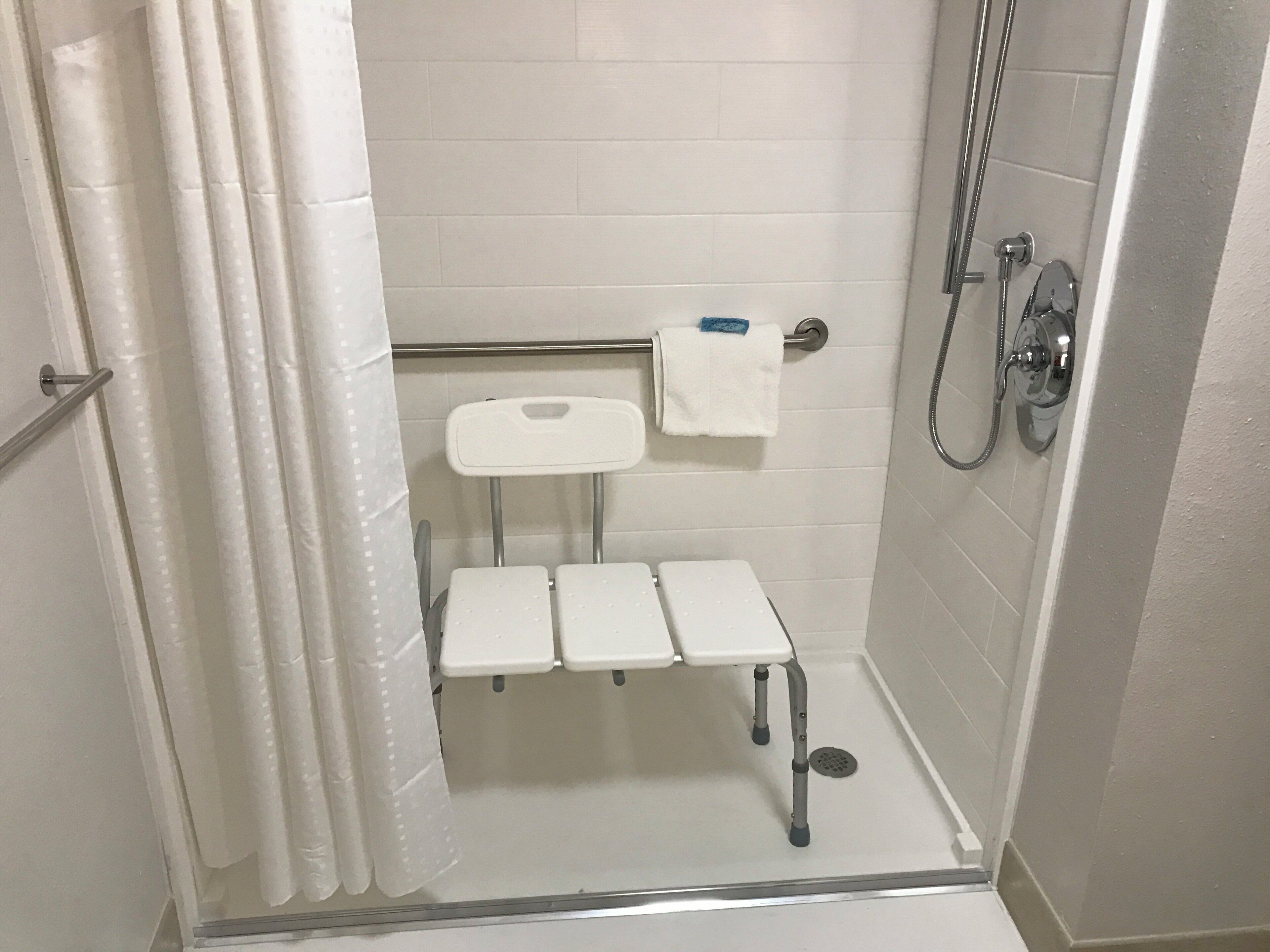 A small, enclosed shower area with a white tiled wall, a showerhead, a handheld shower attachment, and a white towel on a rack.