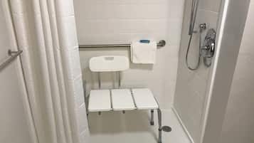A small, enclosed shower area with a white tiled wall, a showerhead, a handheld shower attachment, and a white towel on a rack.