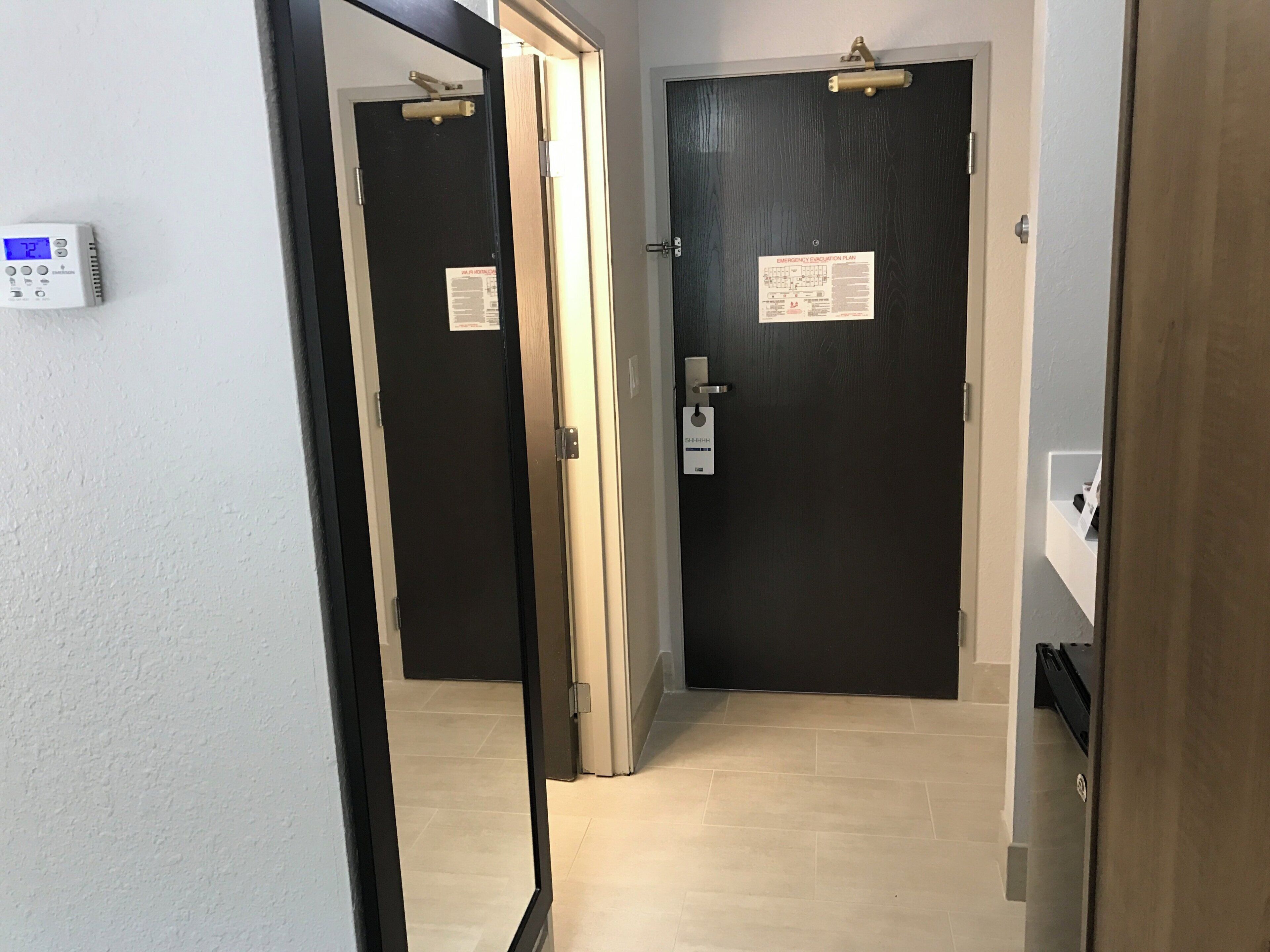 A hallway with two doors, one with a security card reader and a sign, and a thermostat on the wall.
