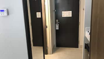 A hallway with two doors, one with a security card reader and a sign, and a thermostat on the wall.