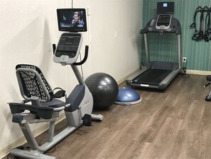 A home gym with an elliptical, a stationary bike, a treadmill, a large exercise ball, and a blue mat.