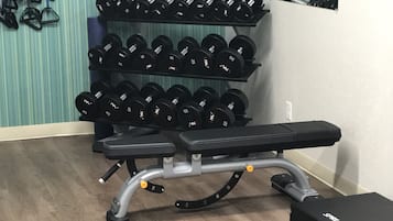 Une salle de sport équipée d’un banc, d’haltères et d’un support à poids.