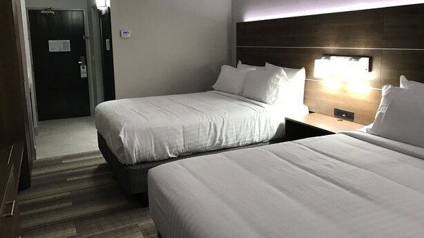 A hotel room with two beds, a dark wooden headboard, a nightstand with a lamp, and a door with a sign. - Holiday Inn Express Naples South I-75 by IHG (Naples)