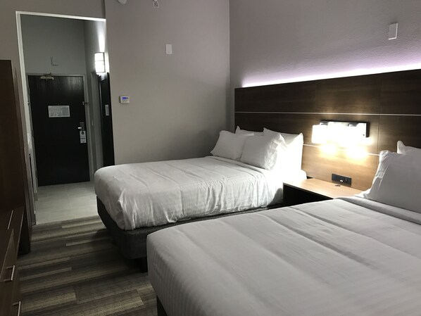 A hotel room with two beds, a dark wooden headboard, a nightstand with a lamp, and a door with a sign.
