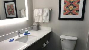 A bathroom with a white sink, a mirror, a toilet, and framed artwork on the walls. - Holiday Inn Express Naples South I-75 by IHG (Naples)