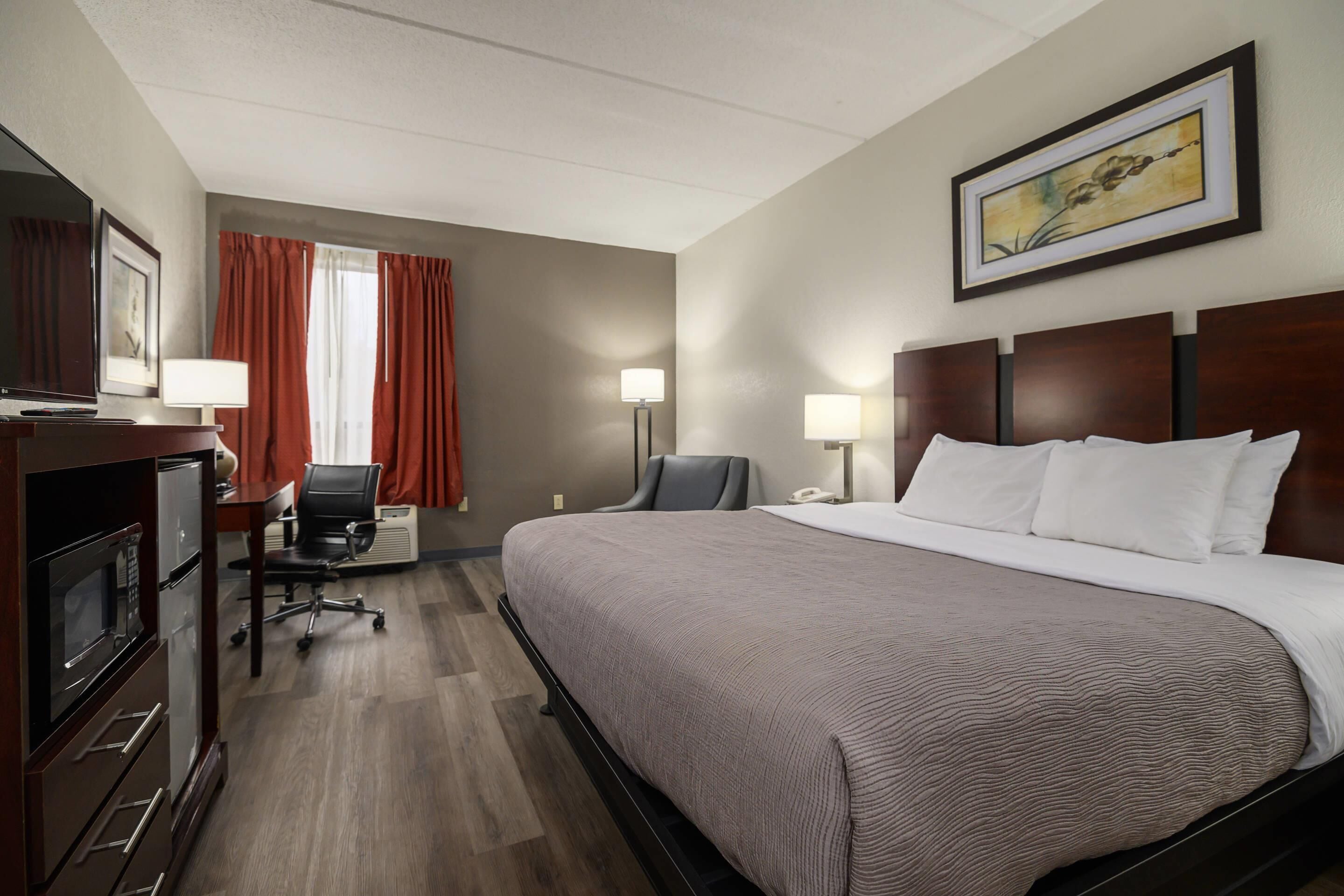 A hotel room with a large bed, a desk with a chair, a TV, and a painting on the wall.