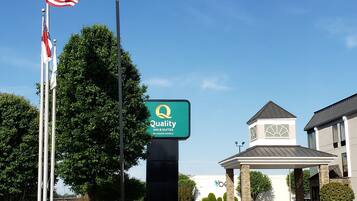 Entrada de un hotel con un letrero de Quality Inn & Suites by Choice Hotels, un asta con la bandera estadounidense y un edificio de diseño moderno.