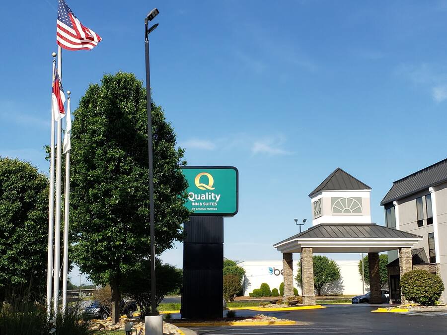 Entrada de un hotel con un letrero de Quality Inn & Suites by Choice Hotels, un asta con la bandera estadounidense y un edificio de diseño moderno.