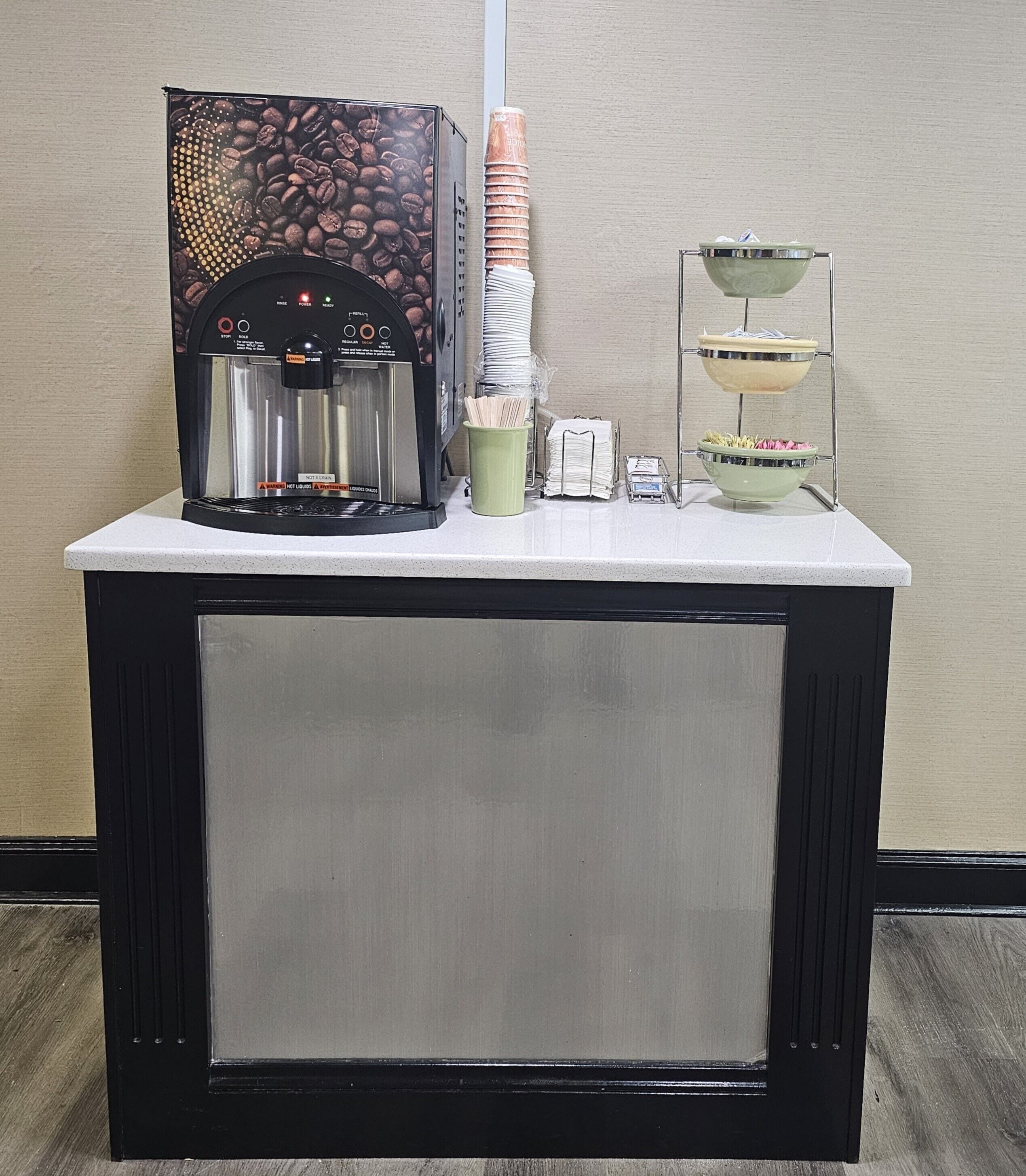 A coffee machine, stacked paper cups, and a small dish rack on a counter.