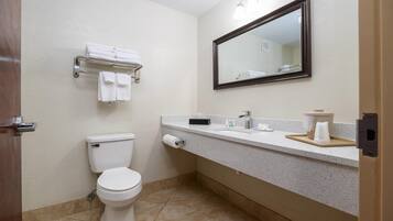 A bathroom with a toilet, towel rack, mirror, and countertop with toiletries.