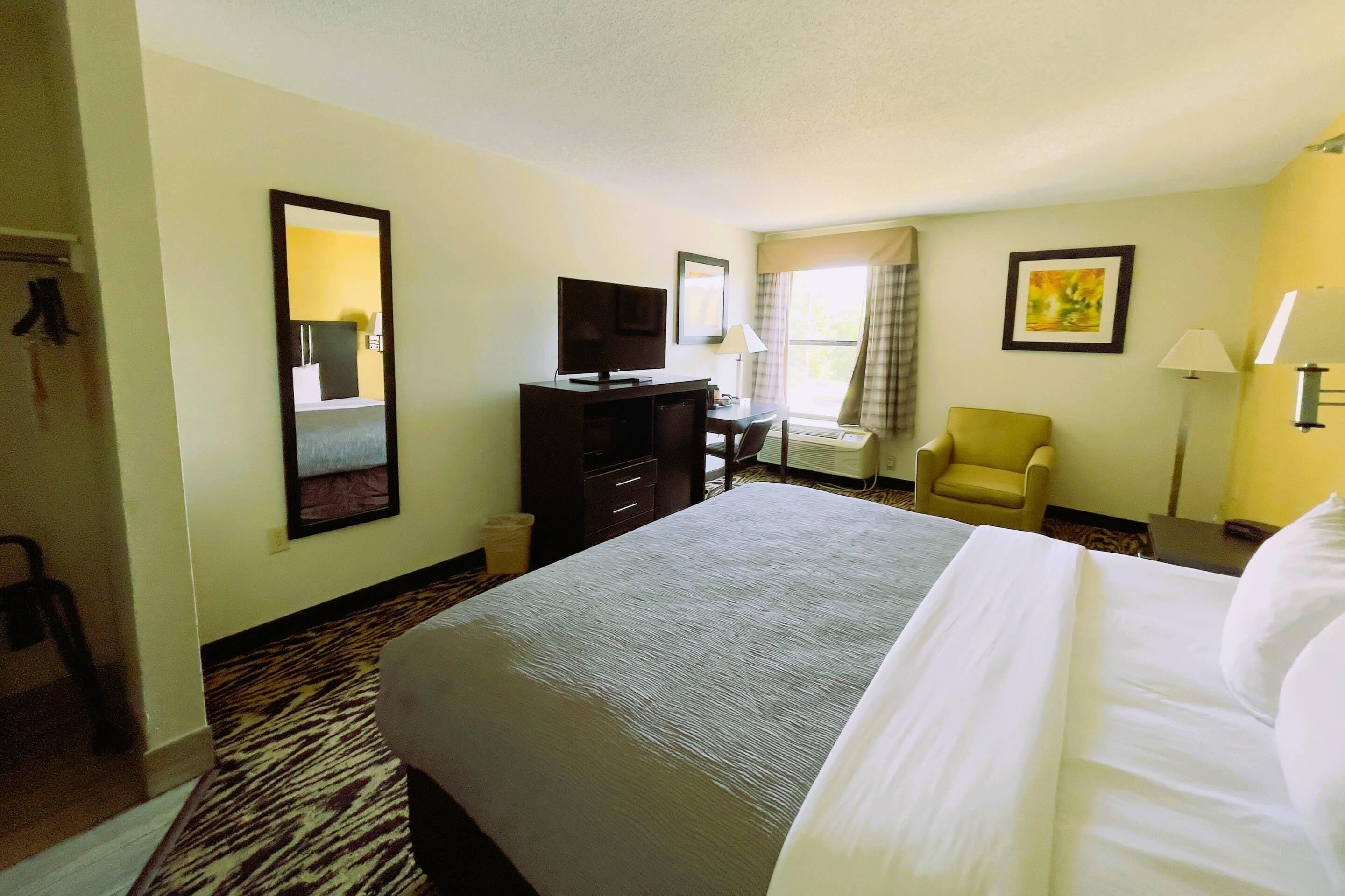A hotel room with a bed, a television, a desk, a chair, and a window with curtains.