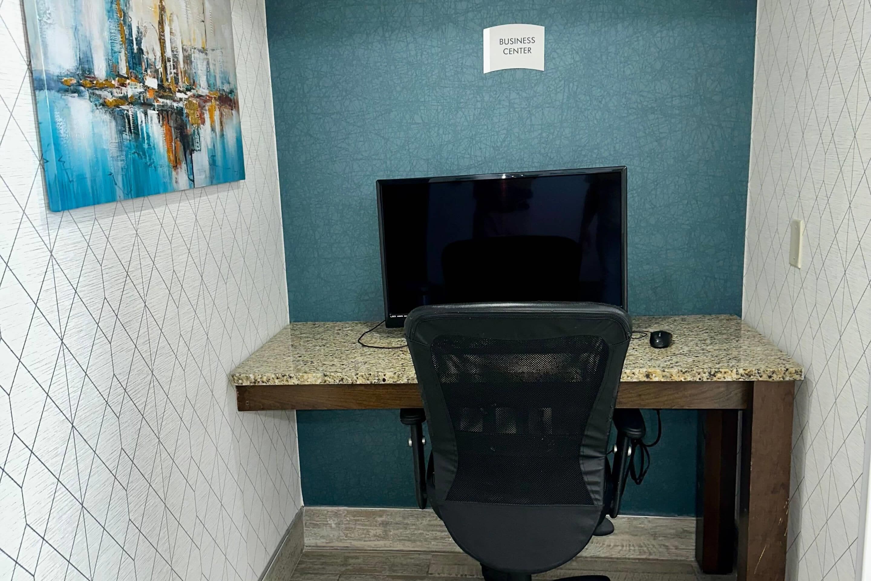 Een business center met een computerbureau, stoel en een schilderij aan de muur.