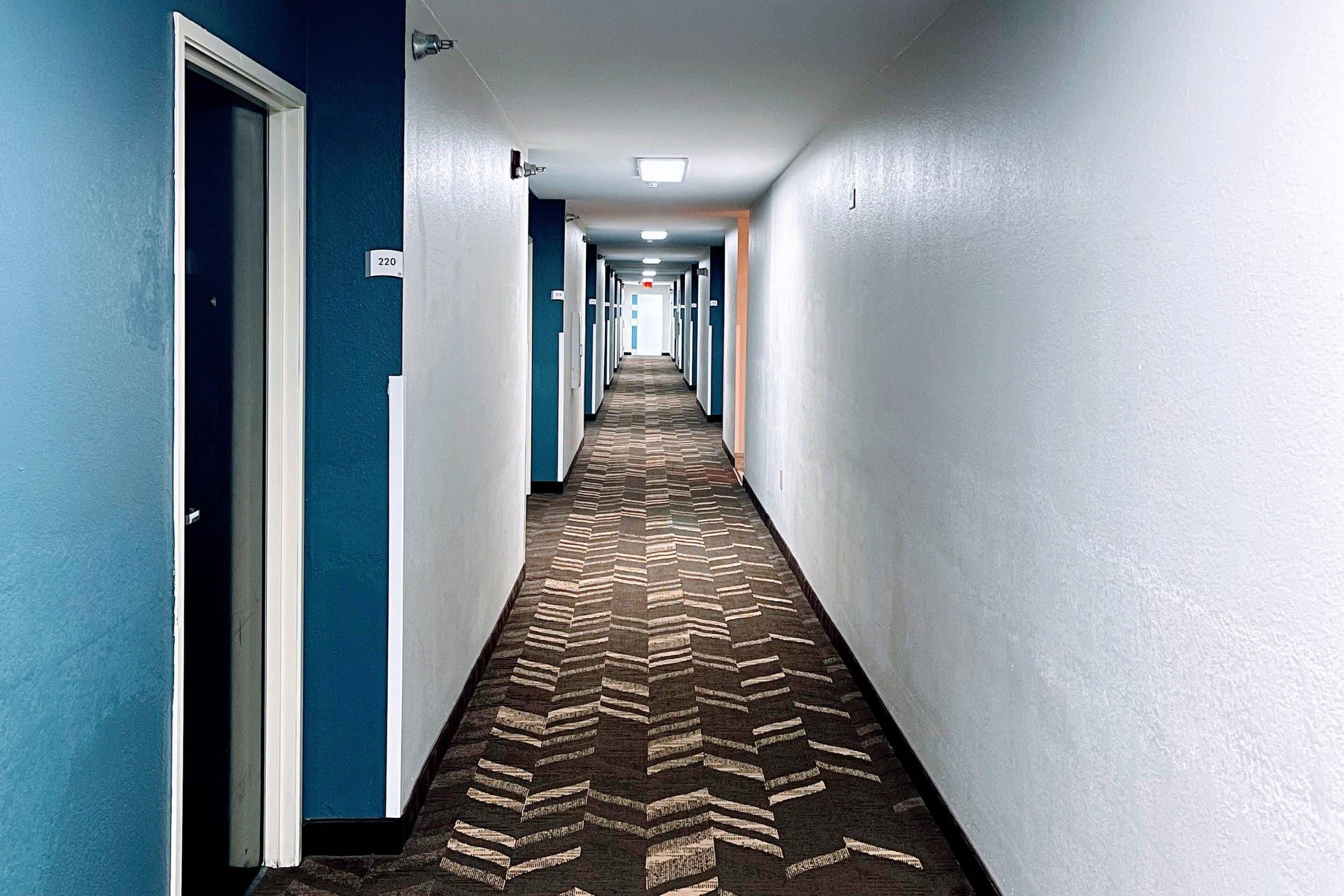 Pasillo de hotel con alfombra estampada, paredes azules y puertas numeradas 220.