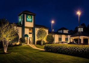 A hotel with a prominent 'Quality Inn & Suites' sign, a well-maintained lawn, and a parking area with cars.