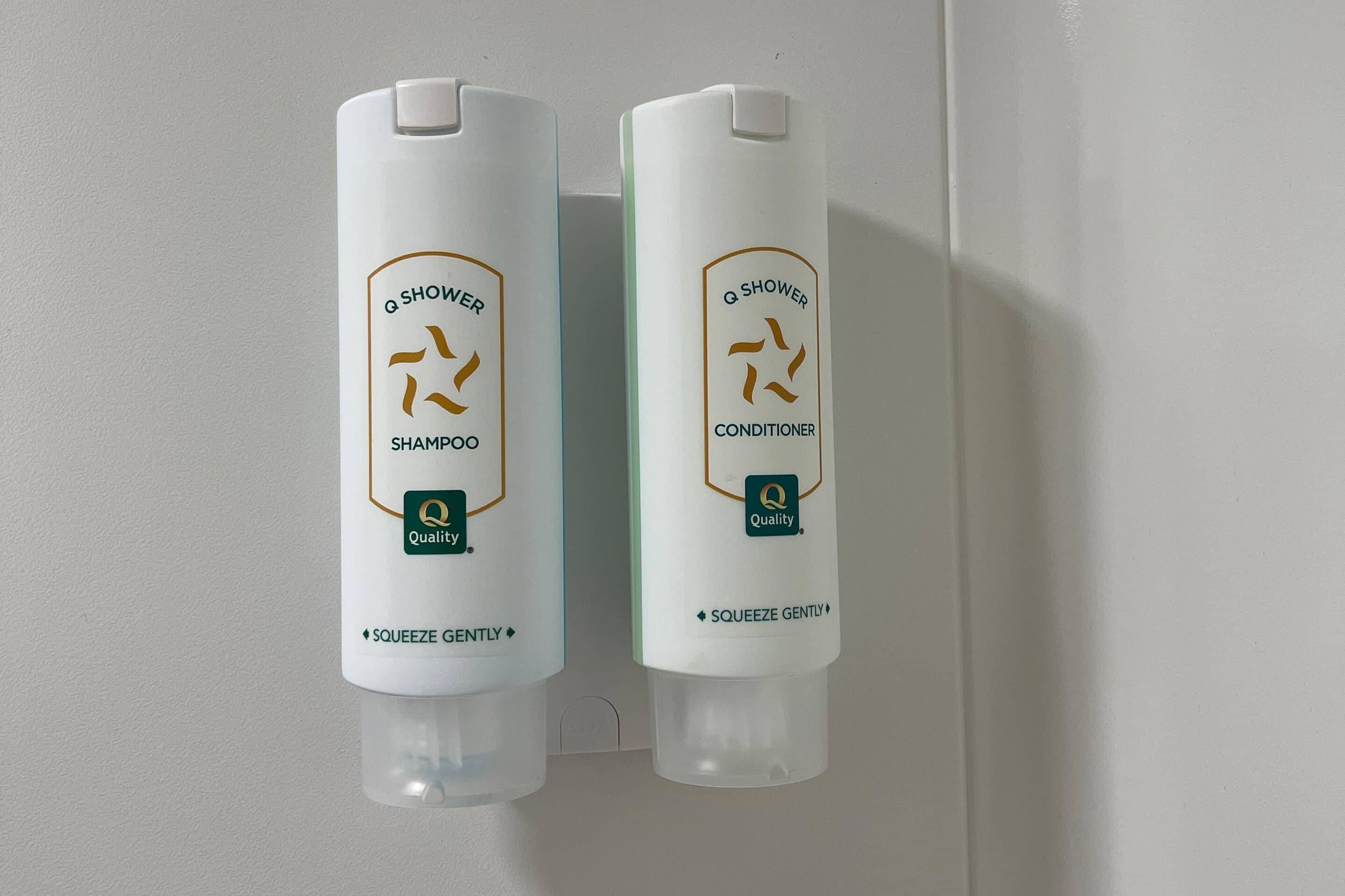 Two bottles of Q Shower shampoo and conditioner mounted on a wall.