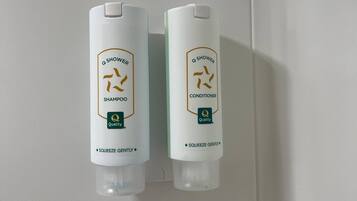 Two bottles of Q Shower shampoo and conditioner mounted on a wall.