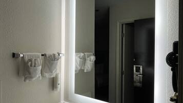 Un baño de hotel con un espejo grande, un lavamanos y un perchero para toallas.