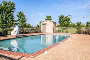 A swimming pool with a brick border, surrounded by a fence, and a small building with a sign.