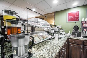 A breakfast area with a coffee machine, a juice dispenser, and a display case with pastries.