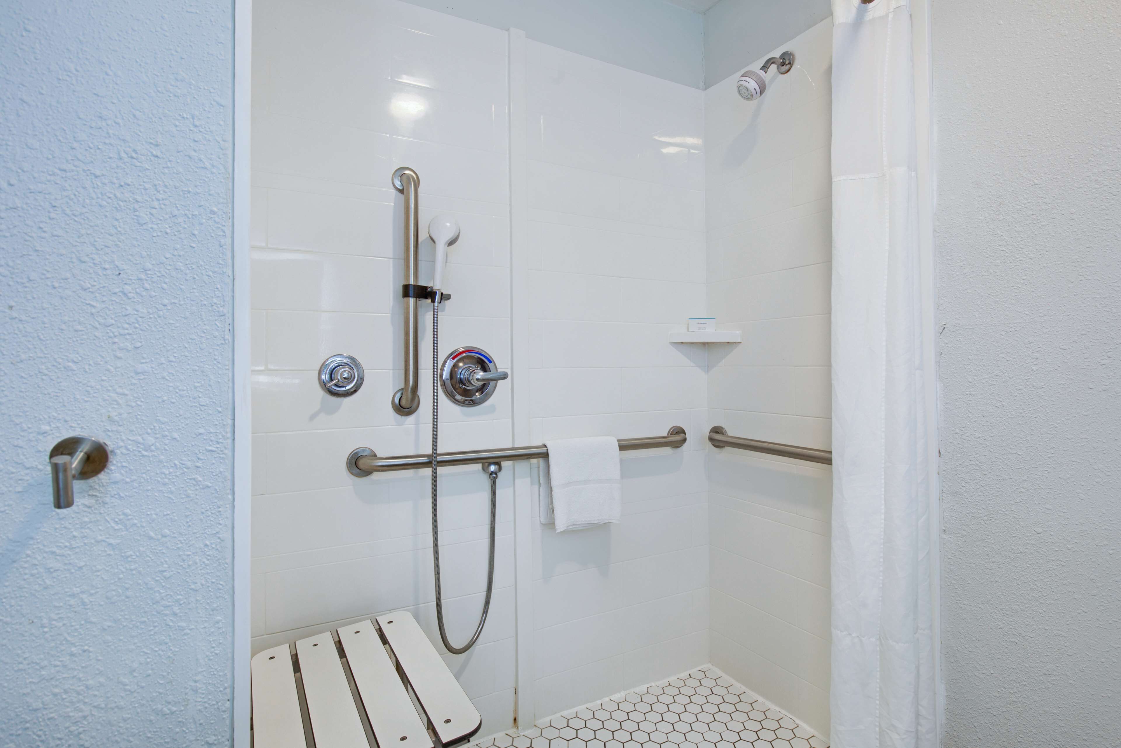 Zona de ducha con pared de azulejos blancos, puerta de cristal, panel de control de ducha y toallero blanco.