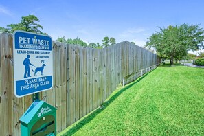 A wooden fence with a sign about pet waste and a green trash bin.