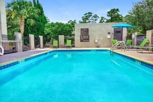 A clear blue pool with a lifeguard sign, no diving allowed, and green lounge chairs.